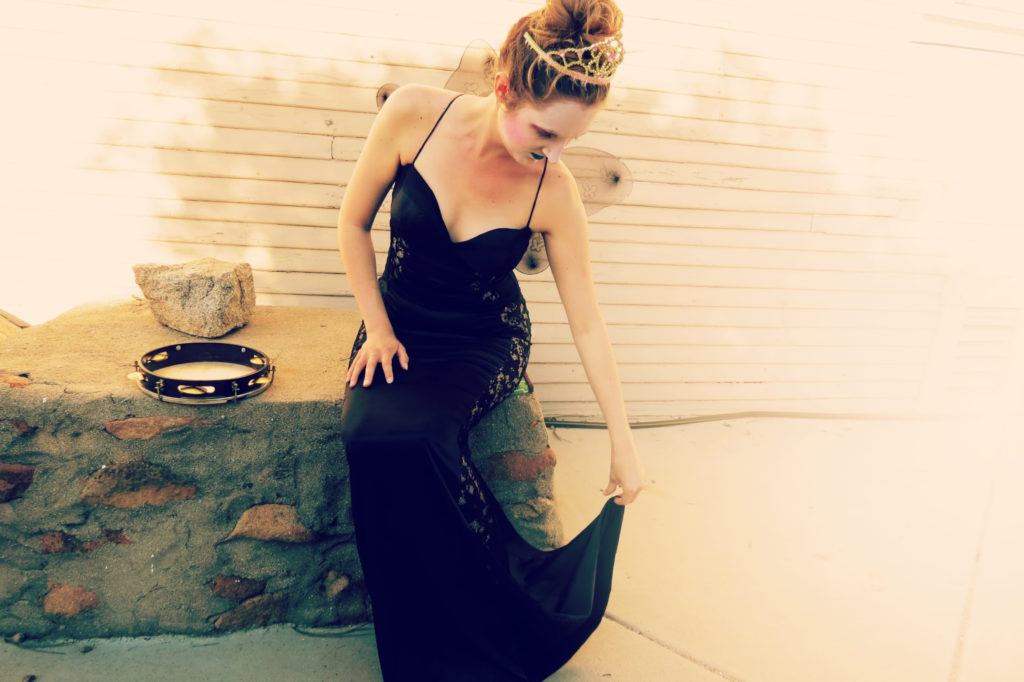 Catherine adjusts the hem of her dress sitting on a ledge next to her pandeiro.