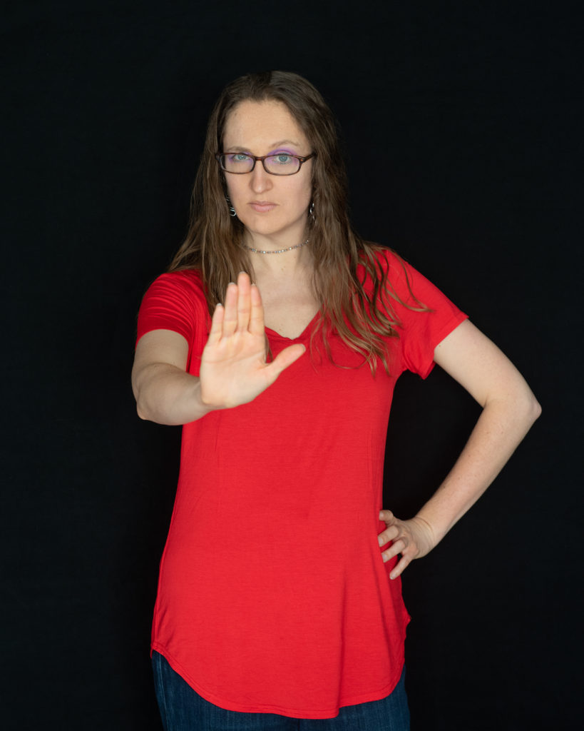 An awkward white lady with glasses in a red shirt making a stop sign with her hand