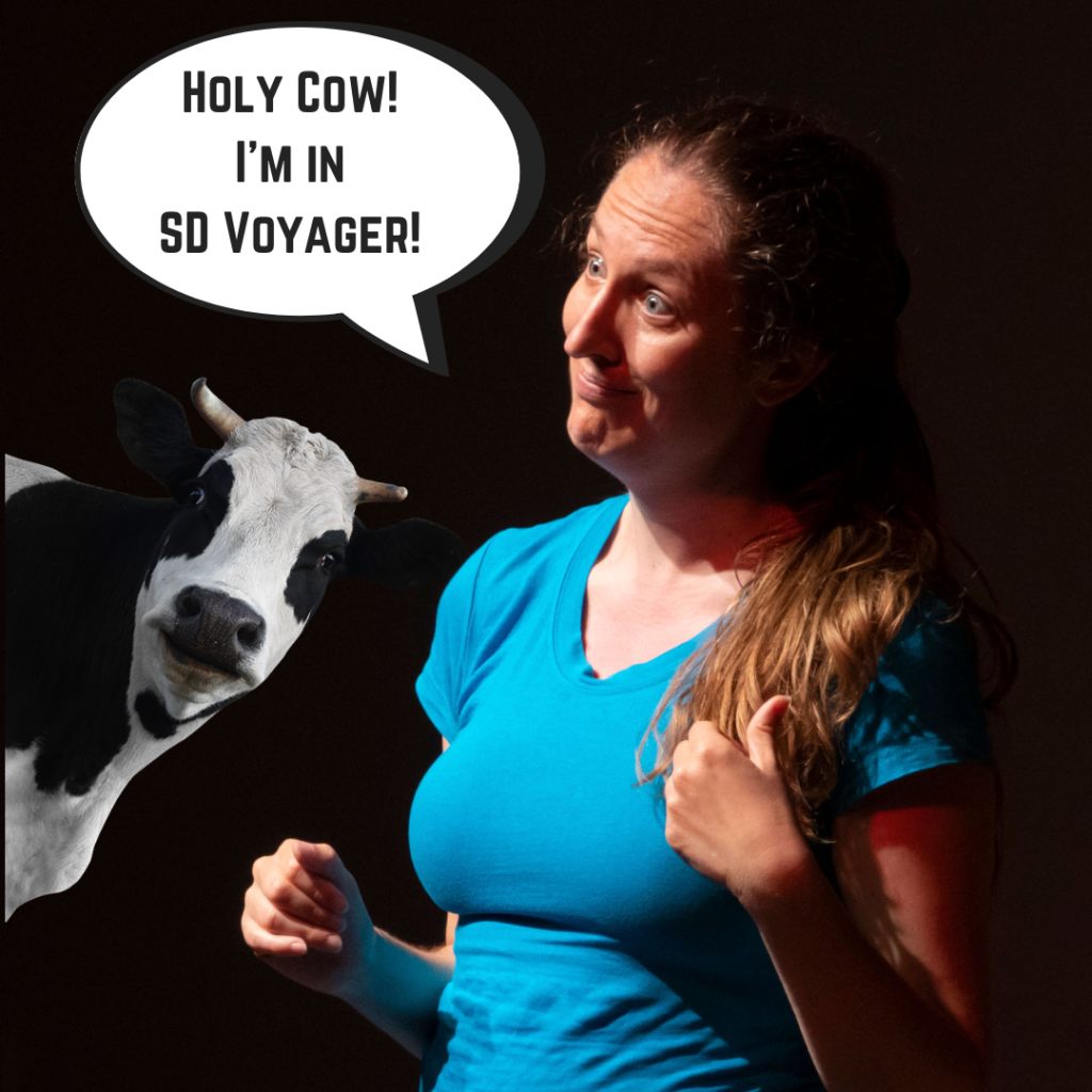 Catherine in a blue shirt with a surprised facial expression. A speech bubble reads, "Holy cow! I'm in SD Voyager!" A cow sticks its head into the image from the left side.