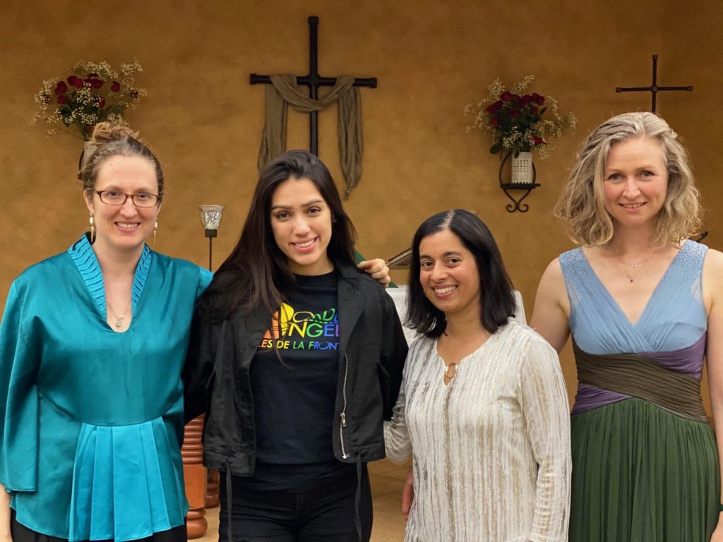 Four women stand shoulder to shoulder in front of a church altar. 